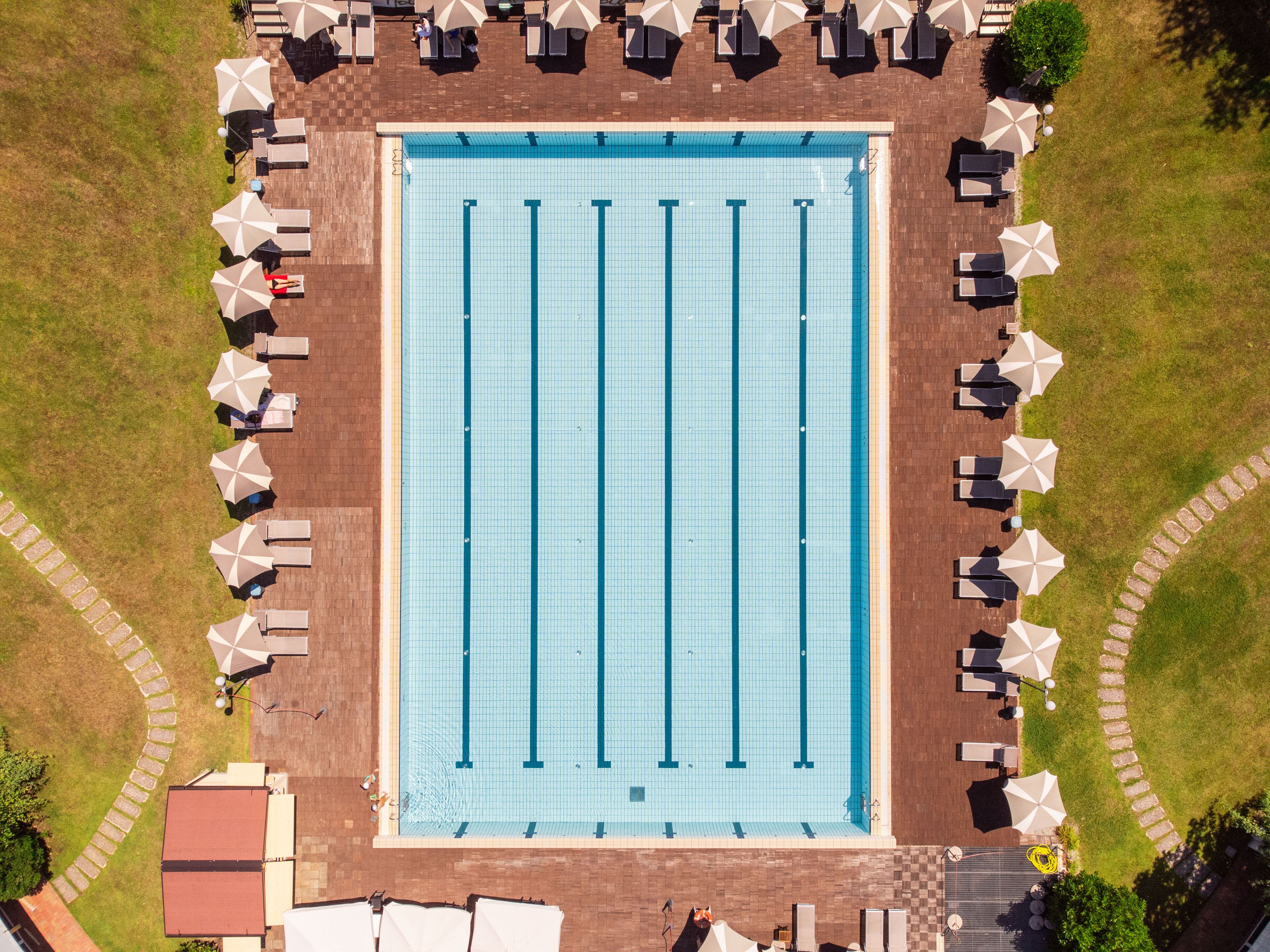 Vista aérea de una piscina con zonas de descanso contiguas y un camino de ladrillo.