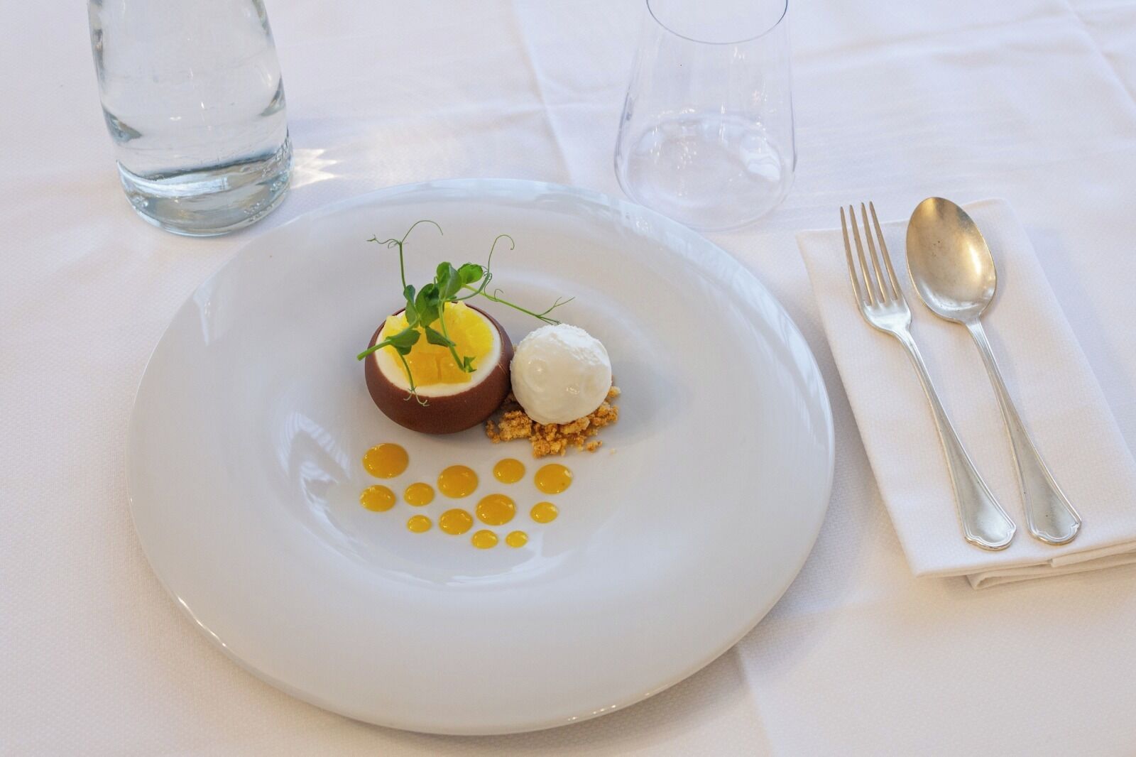 A white plate with a dessert, a fork, and a spoon on a table.