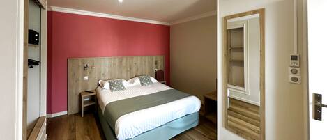 Un dormitorio con cabecera de madera, cama con ropa de cama blanca y verde, mesita de noche y panel de control en la pared.