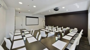 A conference room with a long table, white chairs, and a projector screen. -  Hôtel Arc en Ciel et SPA - Les Sables d'Olonne (Les Sables-d'Olonne)