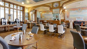 A spacious dining area with wooden tables and chairs, a coffee station, and a mural on the wall. -  Hôtel Arc en Ciel et SPA - Les Sables d'Olonne (Les Sables-d'Olonne)