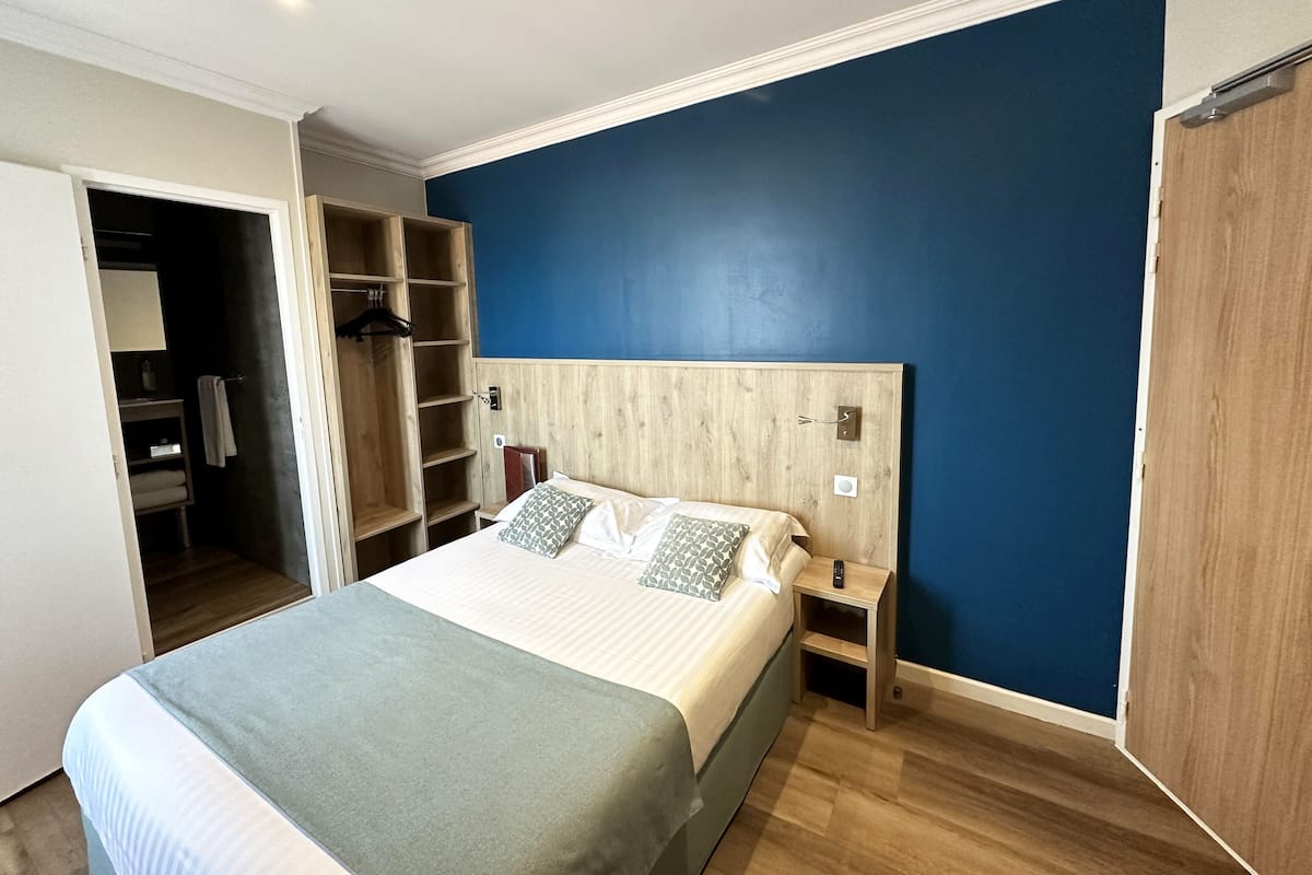 Ein Schlafzimmer mit einem Bett, einem Holzschrank, einem Nachttisch und einer blauen Wand.