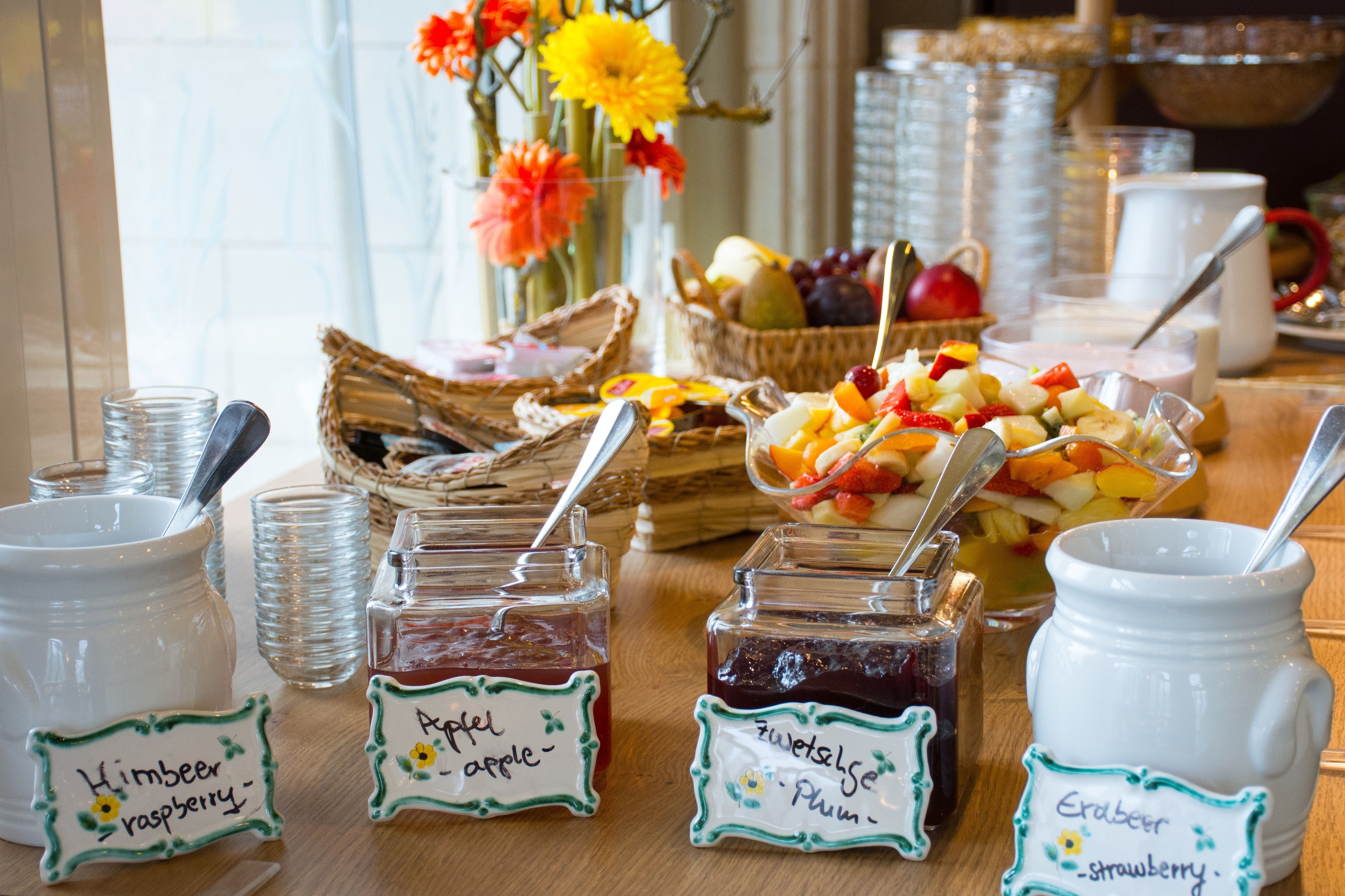 A breakfast buffet with various jams, fruits, and a vase of flowers.