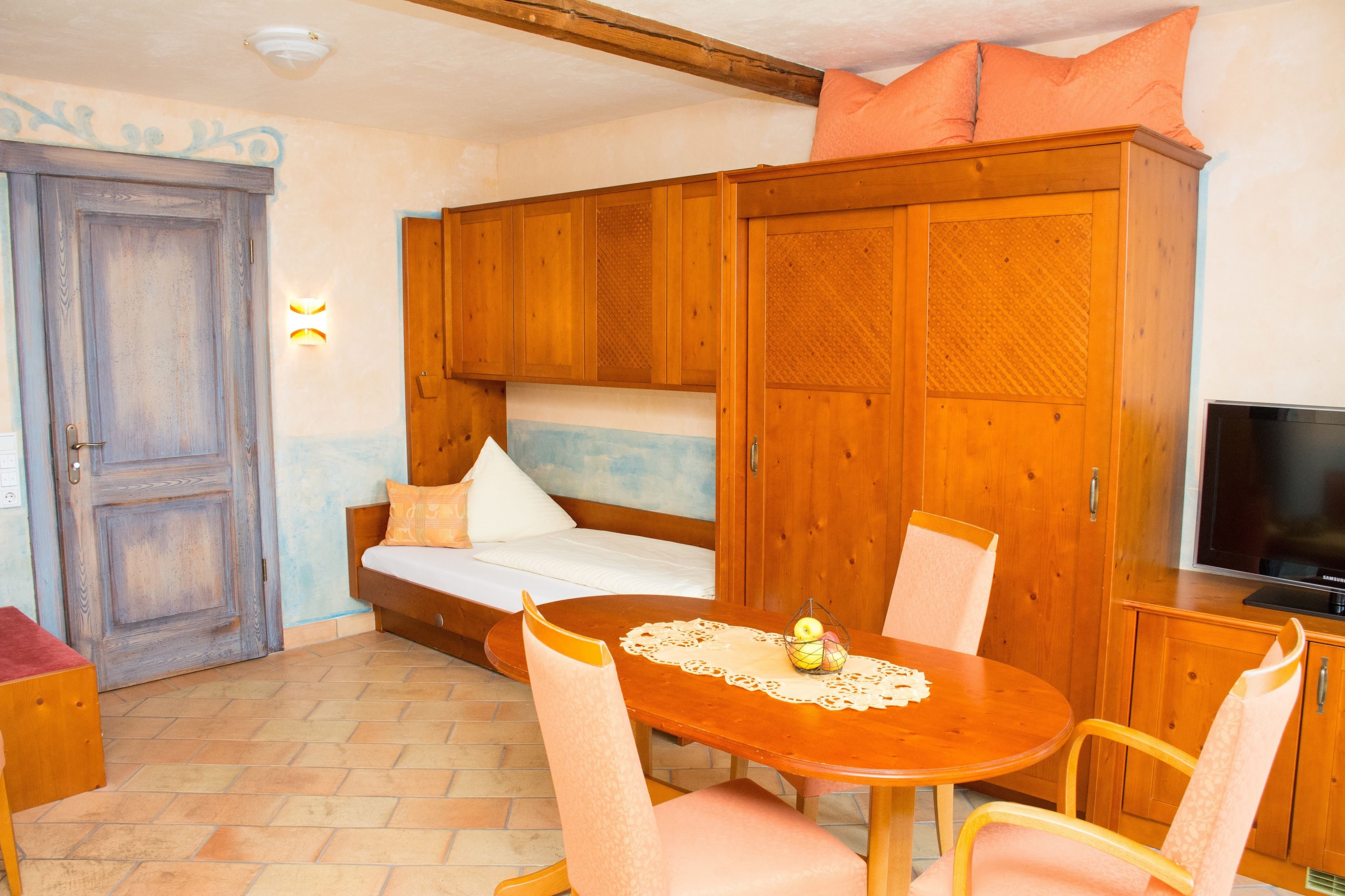A cozy room with a wooden bed, a sofa, a dining table with chairs, and a television.