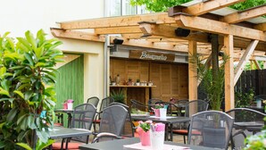 Un café en plein air doté d’une pergola en bois, de tables, de chaises et de plantes en pot.