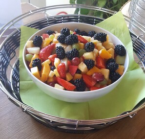 A bowl of mixed fruit salad on a wire basket with a green napkin underneath.
