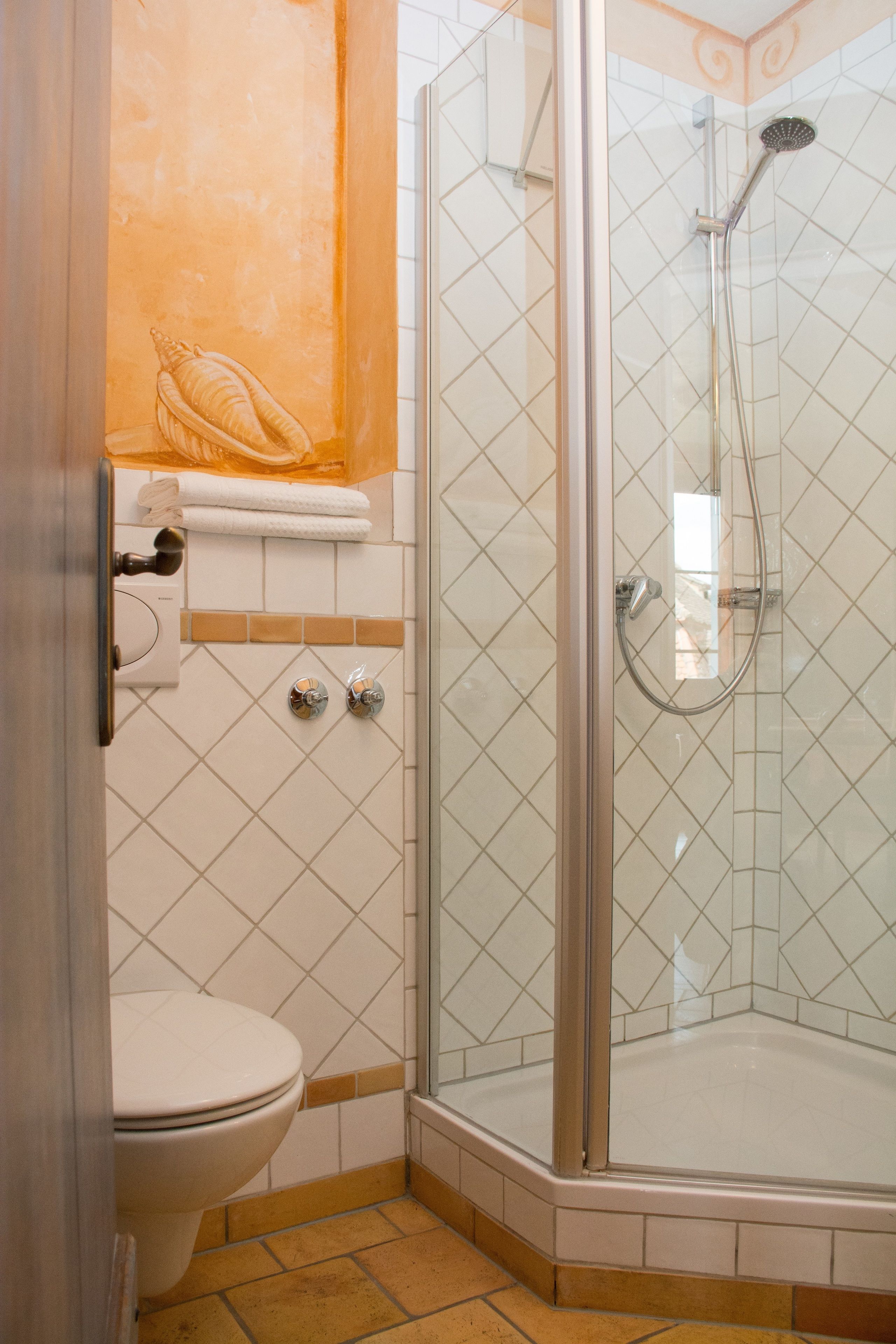 A bathroom with a toilet, a glass-enclosed shower, and a tiled wall.