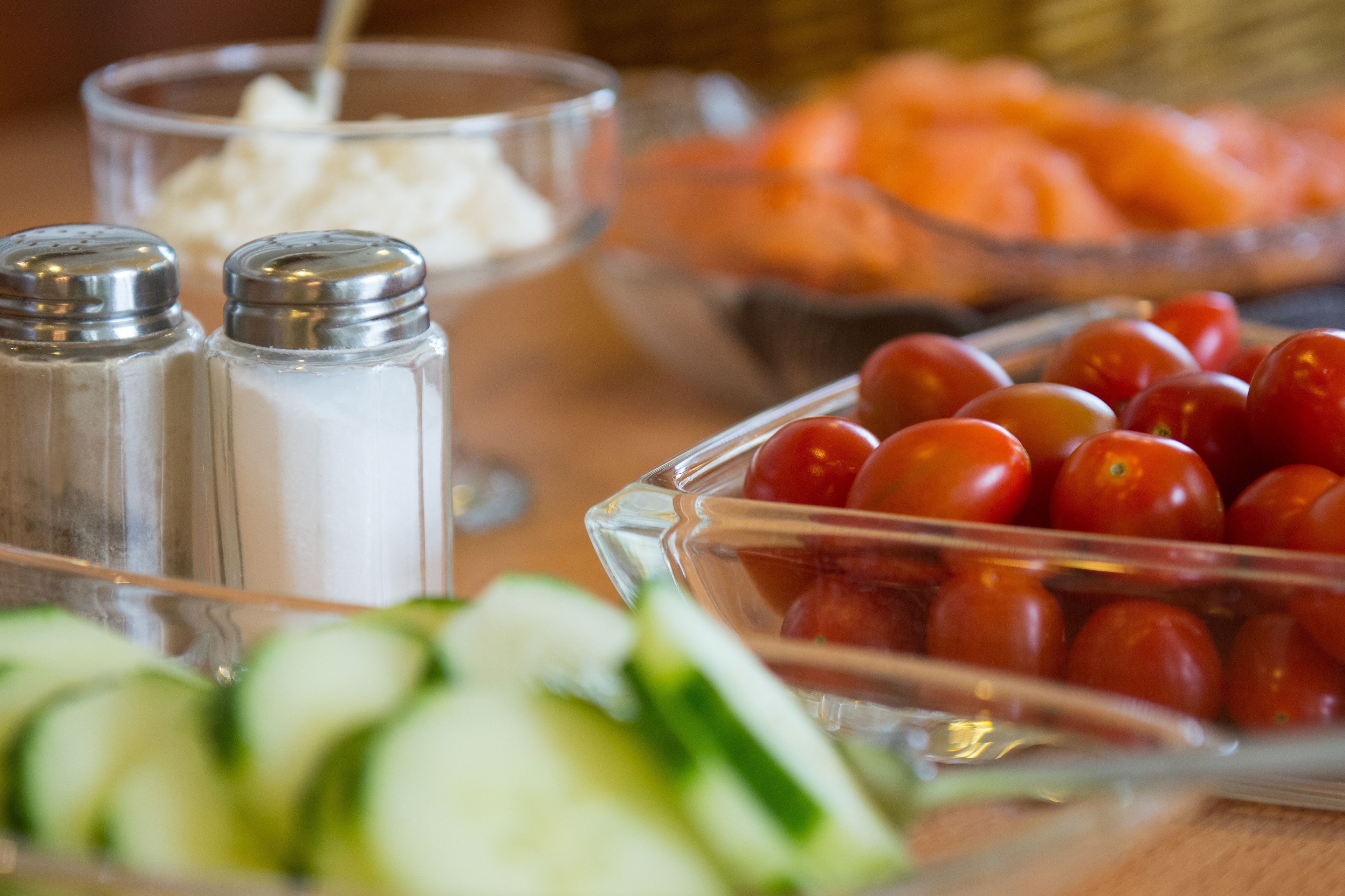 A buffet table with various food items including sliced cucumbers, cherry tomatoes, and a bowl of salmon.