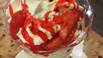 A dessert in a clear glass bowl with whipped cream, strawberries, and a wafer.
