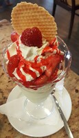 A dessert in a clear glass bowl with whipped cream, strawberries, and a wafer.
