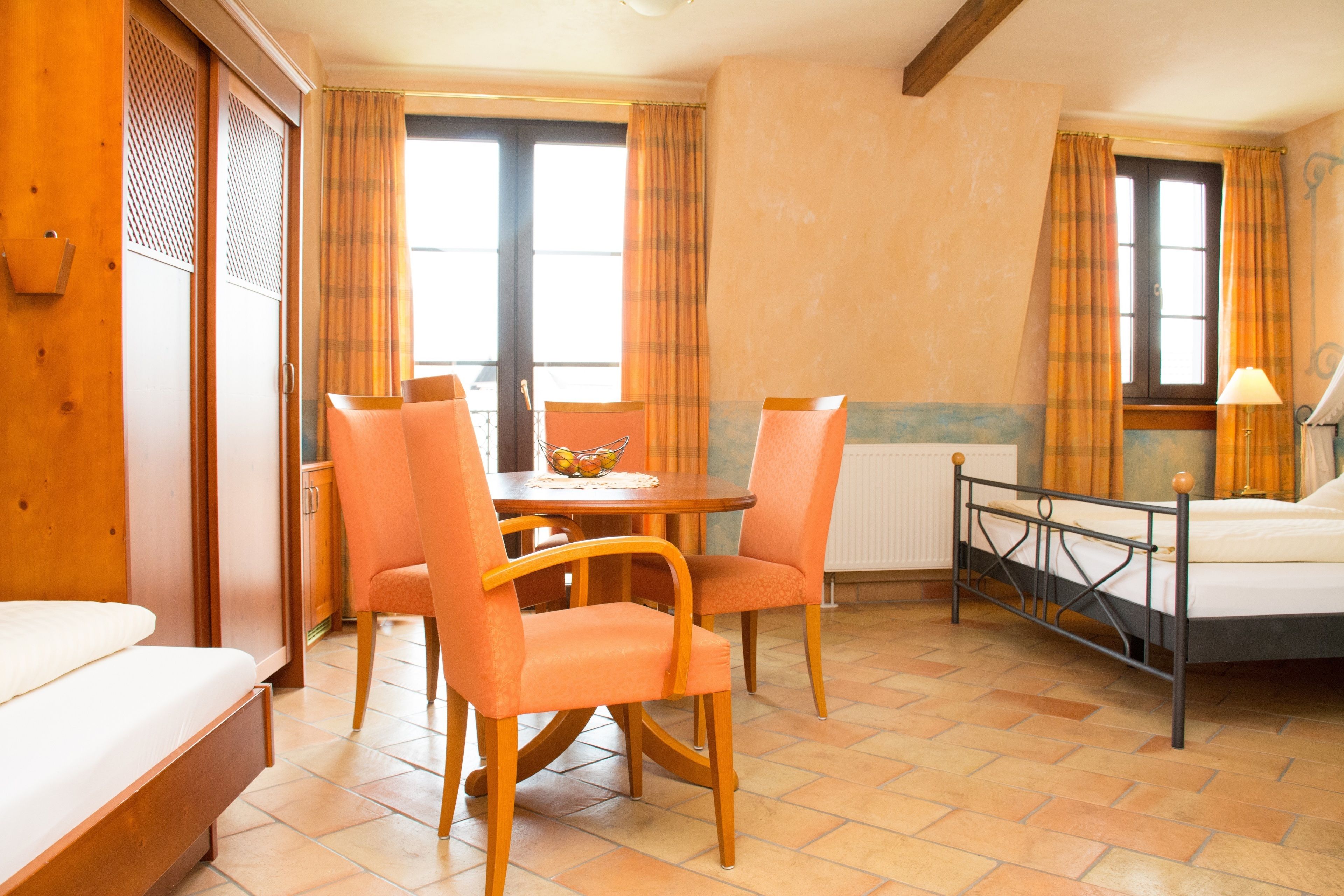 A hotel room with a bed, a dining table with chairs, a small kitchen area, and a window with curtains.