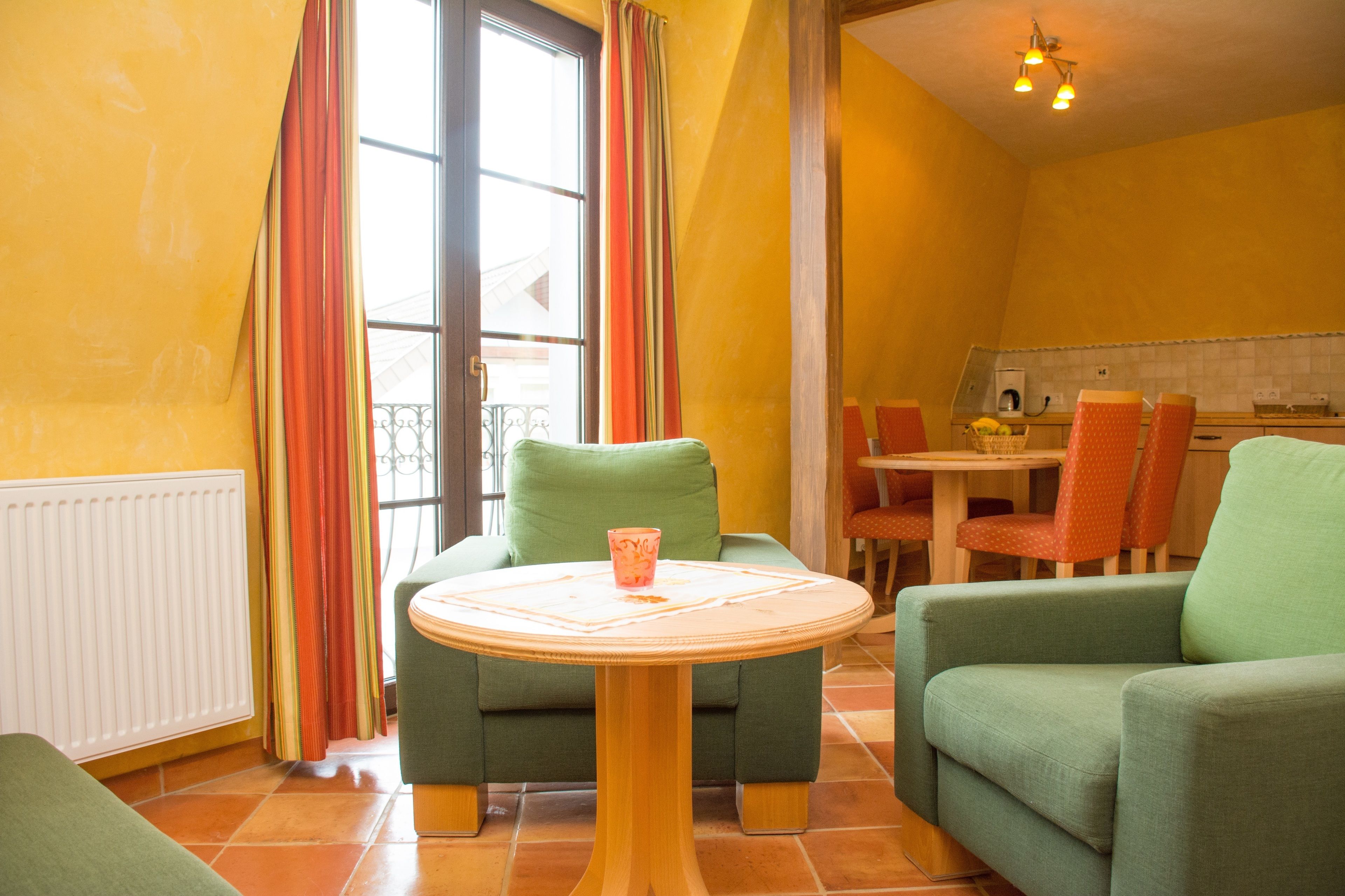 A room with a green sofa, a small round table, and a kitchen area with a dining table and chairs.