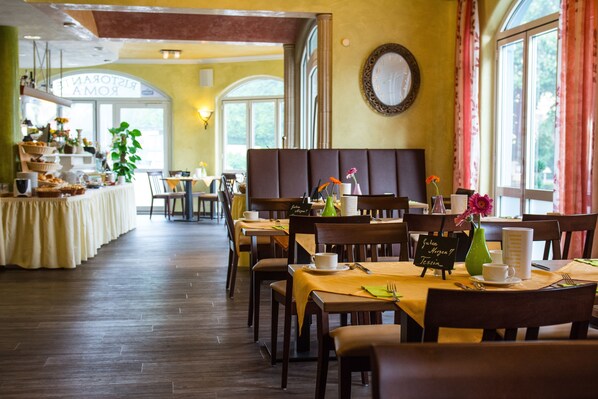 A restaurant with wooden tables and chairs, a buffet area, and a large window with curtains.