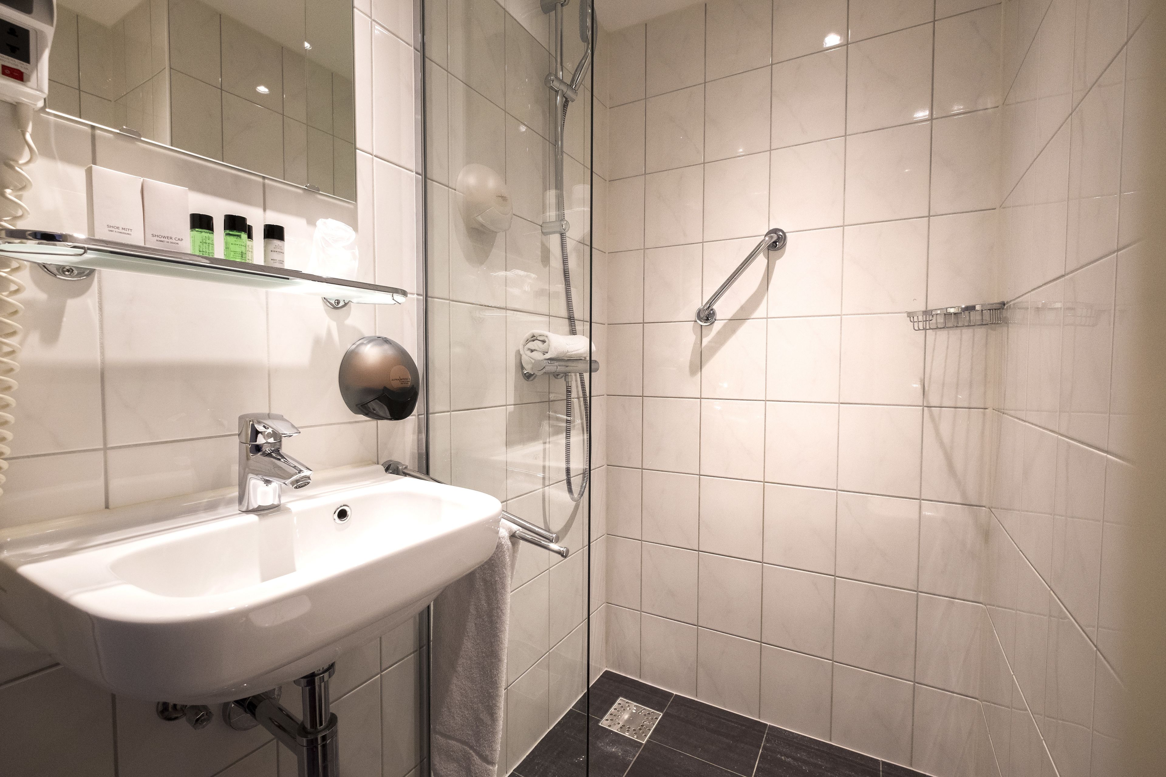A modern bathroom with a glass-enclosed shower, a white sink, and a shelf with toiletries.