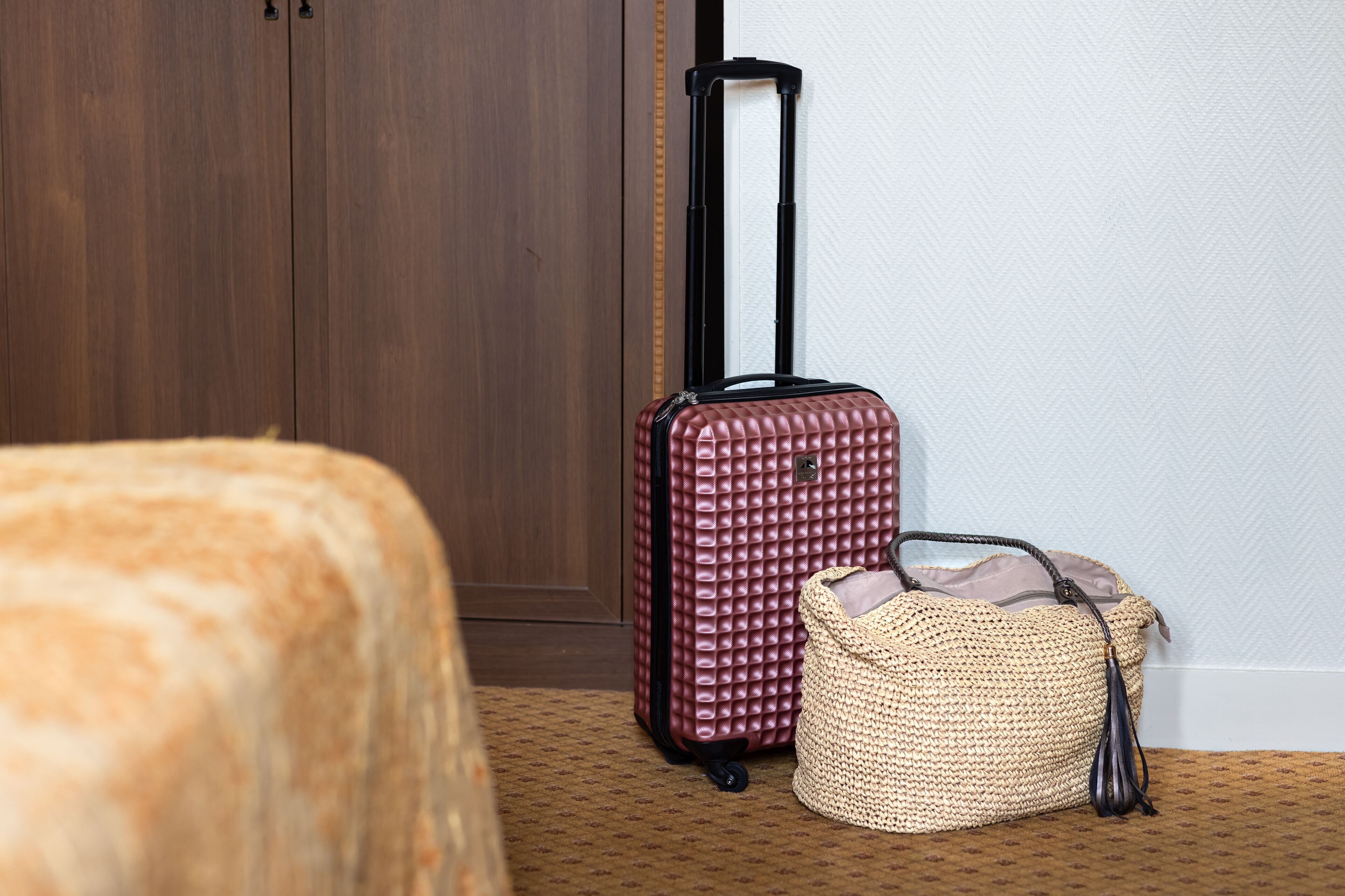 A room with a wooden wardrobe, a red suitcase, and a woven bag.