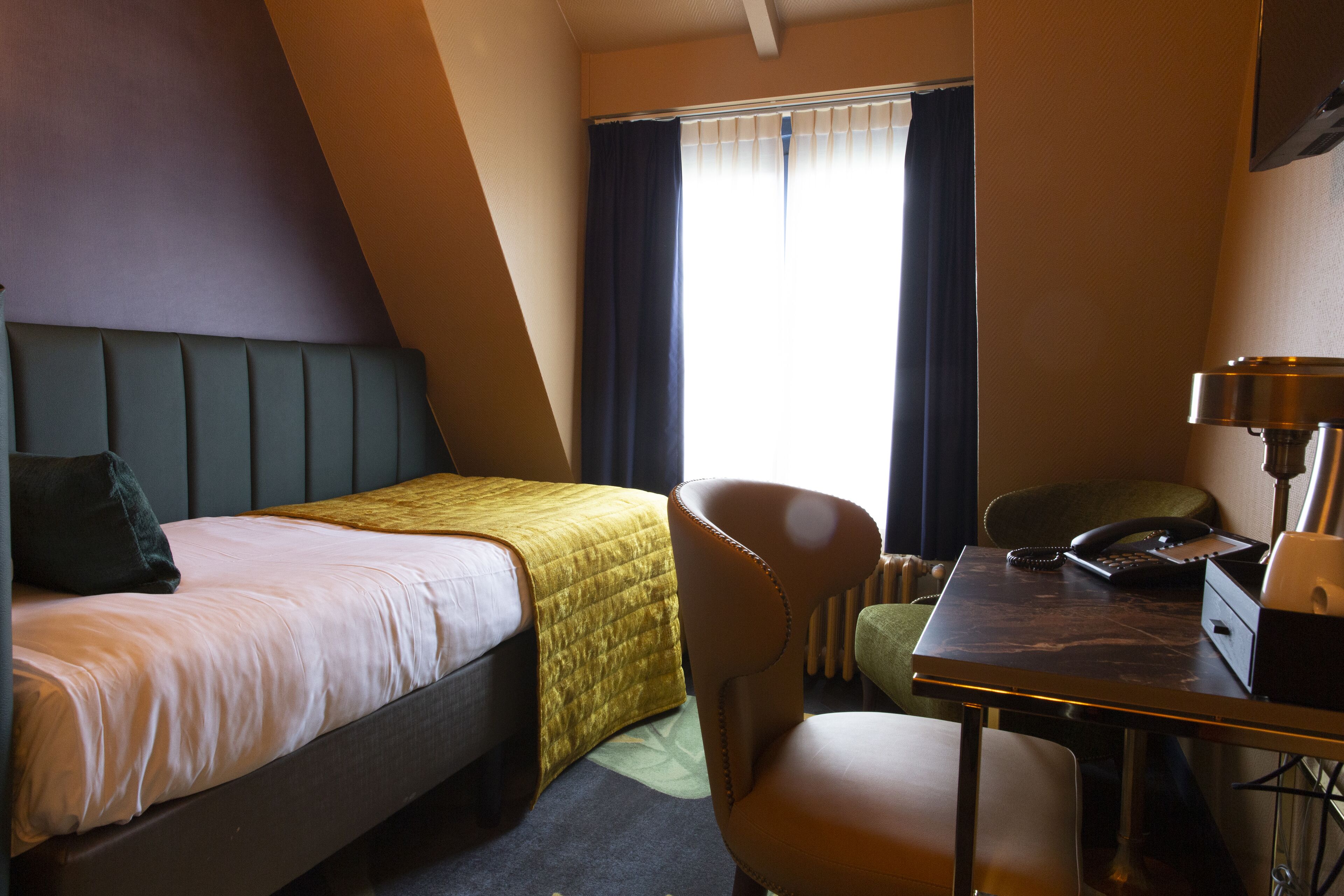 A hotel room with a bed, a desk, a chair, and a window with curtains.