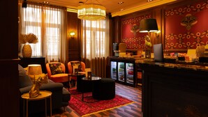 A hotel lobby with a sofa, armchairs, a coffee table, a red rug, a minibar, and a decorative wall. - Hotel Aalders (Amsterdam)
