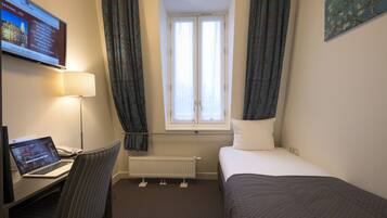 Een hotelkamer met een bed, een bureau met een laptop, een raam met gordijnen en een radiator.