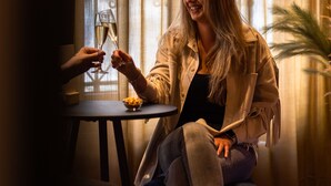 A person sitting at a table with a glass of wine, near a window with sheer curtains. - Hotel Aalders (Amsterdam)