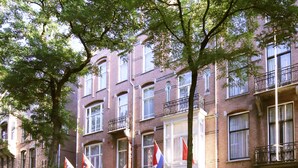 A row of brick buildings with multiple windows and balconies, some with flags. - Hotel Aalders (Amsterdam)