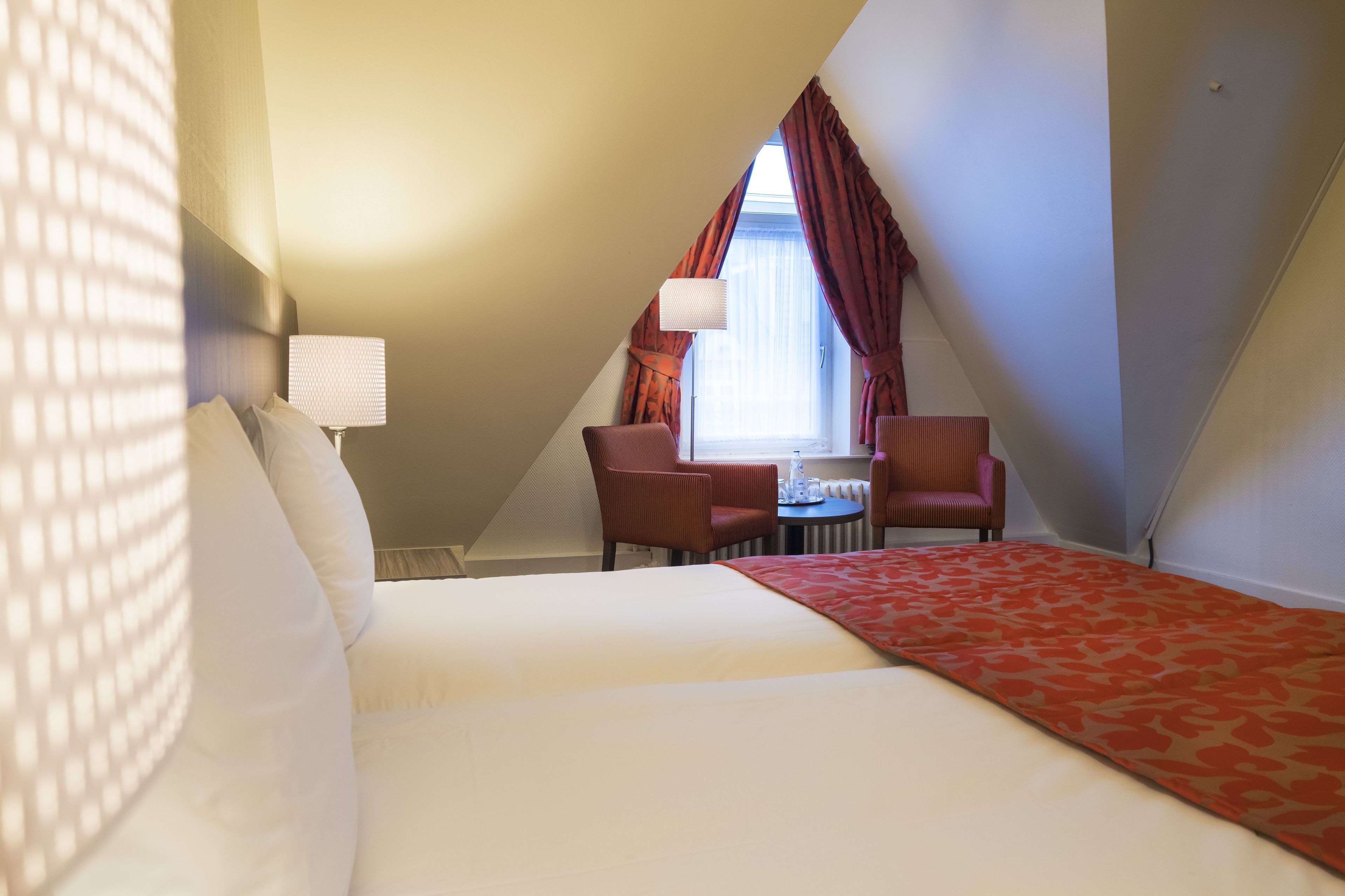 Habitación de hotel con una cama, dos sillas, una mesita y una ventana con cortinas.