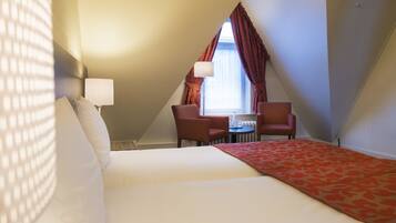 Habitación de hotel con una cama, dos sillas, una mesita y una ventana con cortinas.