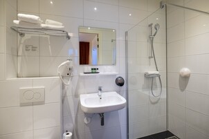 Un baño moderno con cabina de ducha de vidrio, un lavamanos blanco y un perchero para toallas.