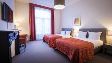 Une chambre d’hôtel avec deux lits, un bureau, une chaise, un radiateur et un téléviseur.