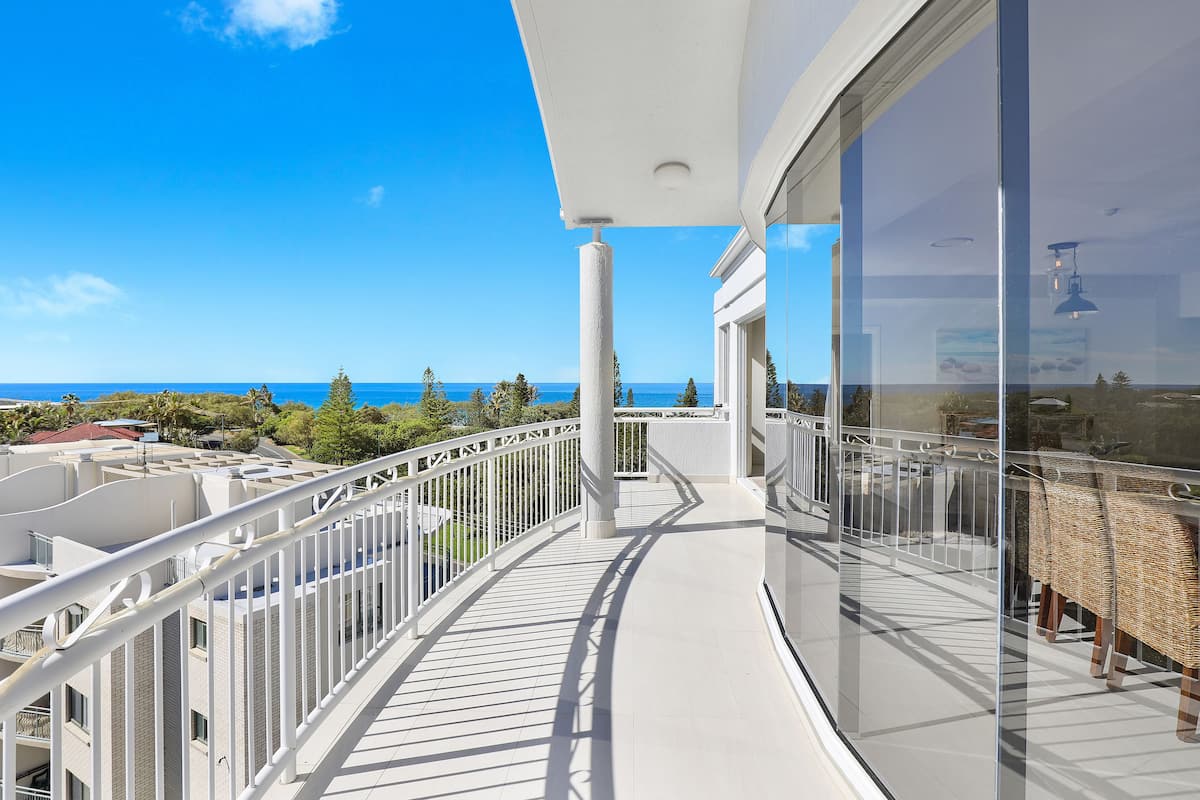 A balcony with a view of the sea, white railings, and a glass door.