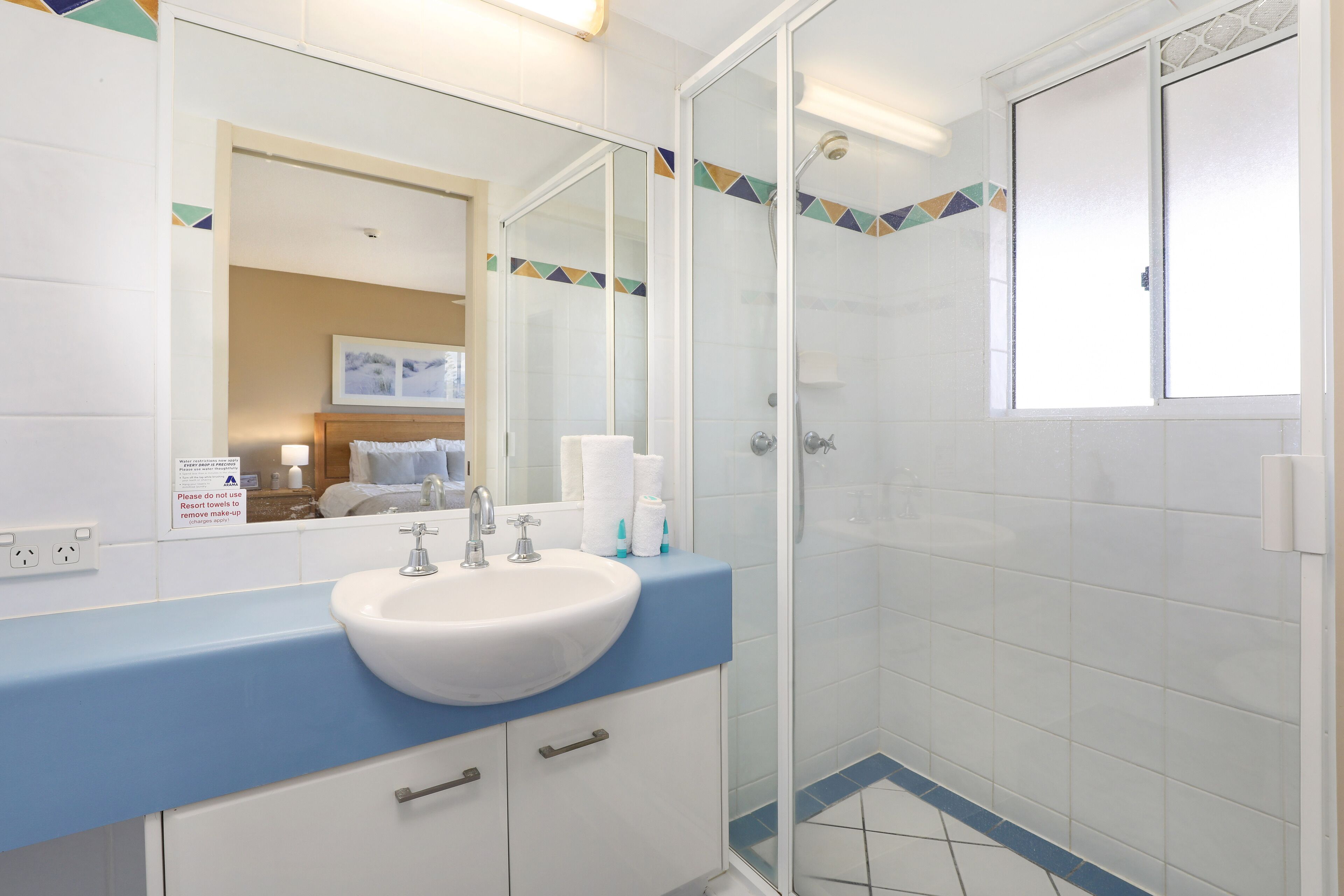 Ein Badezimmer mit einem weißen Waschbecken, einer blauen Arbeitsplatte und einer Duschkabine aus Glas.