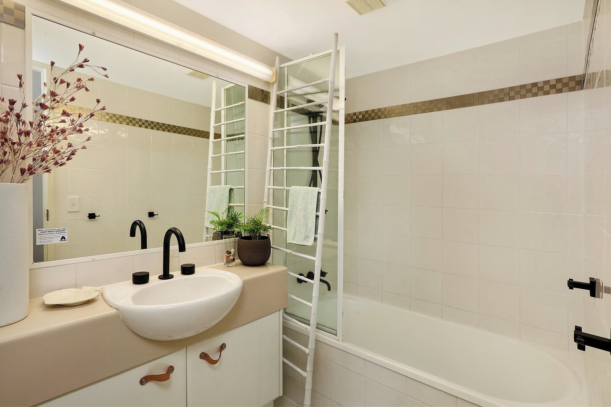 A bathroom with a white sink, a mirror, a towel rack, and a shower area.