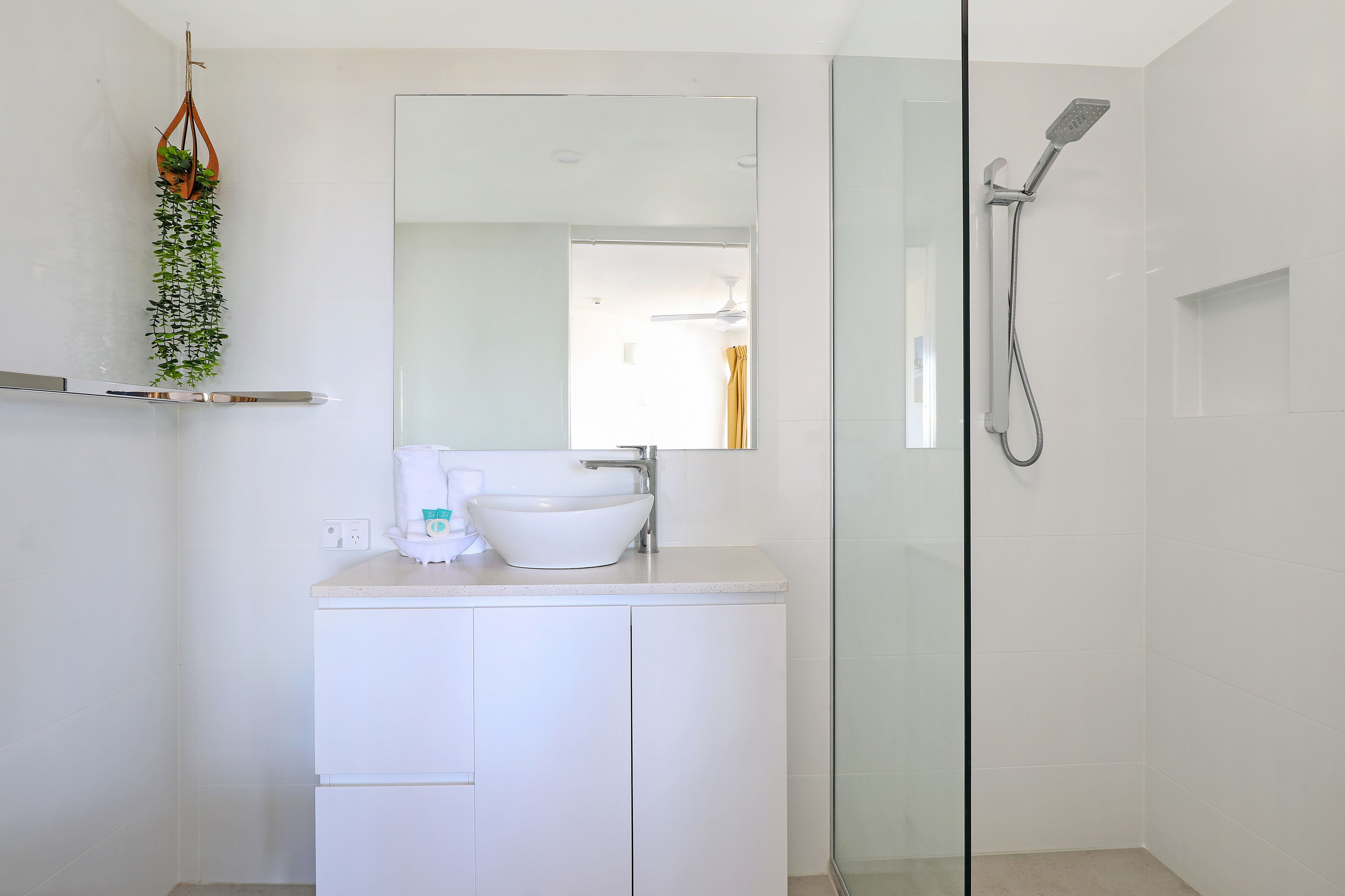 Une salle de bain moderne avec une douche à parois de verre, un lavabo blanc et un miroir au-dessus.
