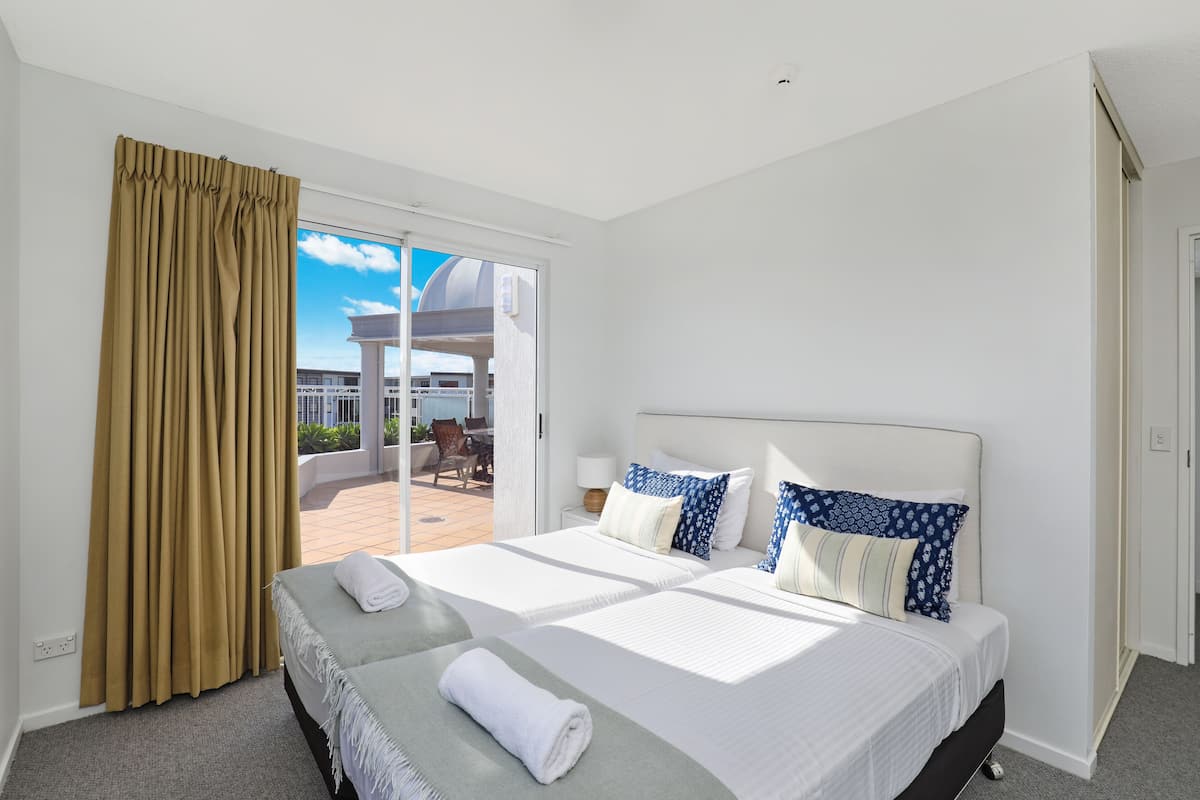 A hotel room with two beds, a balcony with a view of a building, and a sliding glass door.