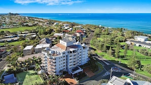 A beachfront hotel with multiple balconies, a tennis court, and a view of the ocean.