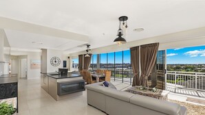 A modern living room with a large sofa, a dining area, and a kitchen. There is a balcony with a view of the city.