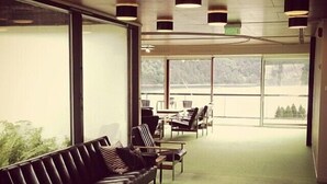 Un intérieur moderne avec un canapé en cuir noir, des tables, des chaises et de grandes fenêtres donnant sur la verdure.