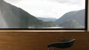 Une vue depuis une fenêtre donnant sur un intérieur en bois, avec un paysage montagneux et un lac en contrebas.
