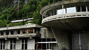 Un grand bâtiment circulaire en béton, doté d’un toit plat et entouré d’une forêt verdoyante et dense.