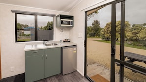 Une cuisine compacte équipée d’un four à micro-ondes, d’un évier et d’un lave-vaisselle, donnant sur une terrasse avec vue sur un parc.