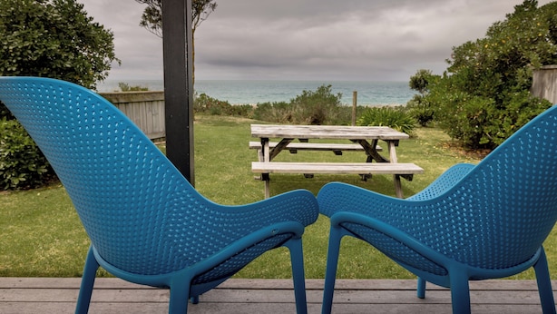 Une terrasse avec deux chaises bleues donnant sur une table de pique-nique en bois et offrant une vue sur l’océan.
