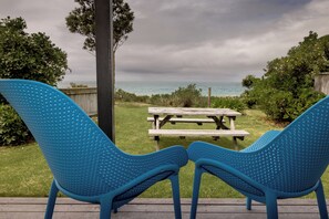 A deck with two blue chairs facing a wooden picnic table and a view of the ocean. - Napier Beach TOP 10 Holiday Park (Napier)