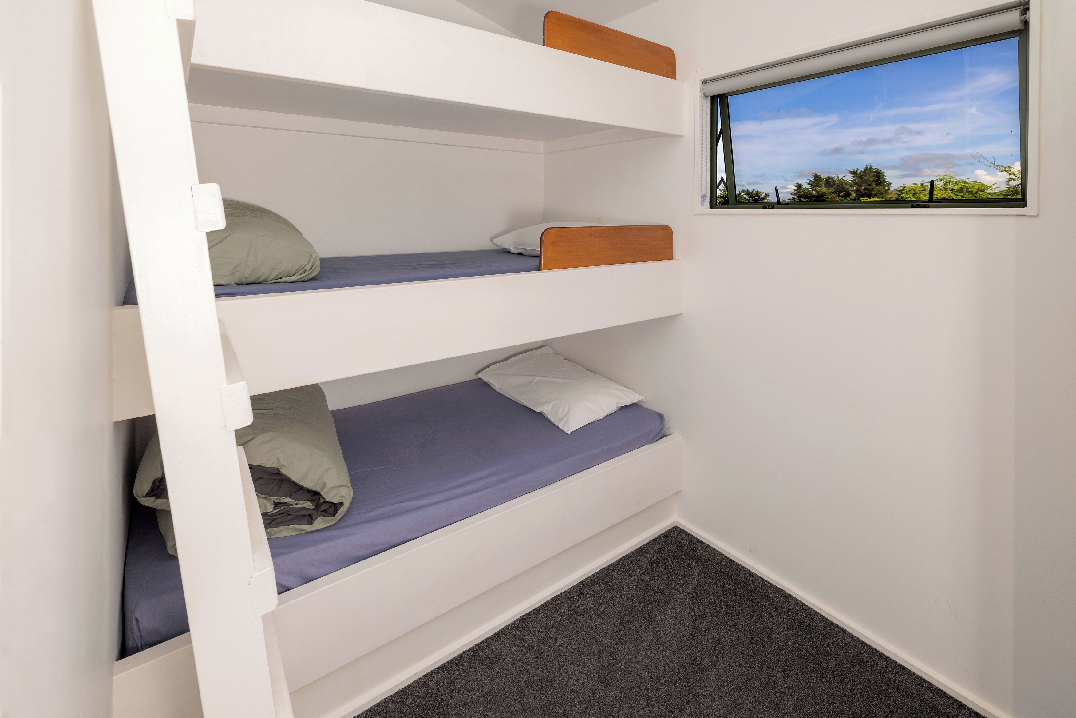A bunk bed with three levels, a window with a view of greenery, and a carpeted floor.