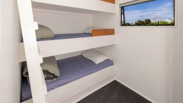 A bunk bed with three levels, a window with a view of greenery, and a carpeted floor.