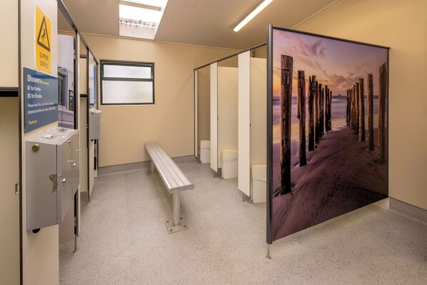 Un baño con un banco, un cartel que indica el precio de las duchas y un cuadro grande de un muelle de madera.