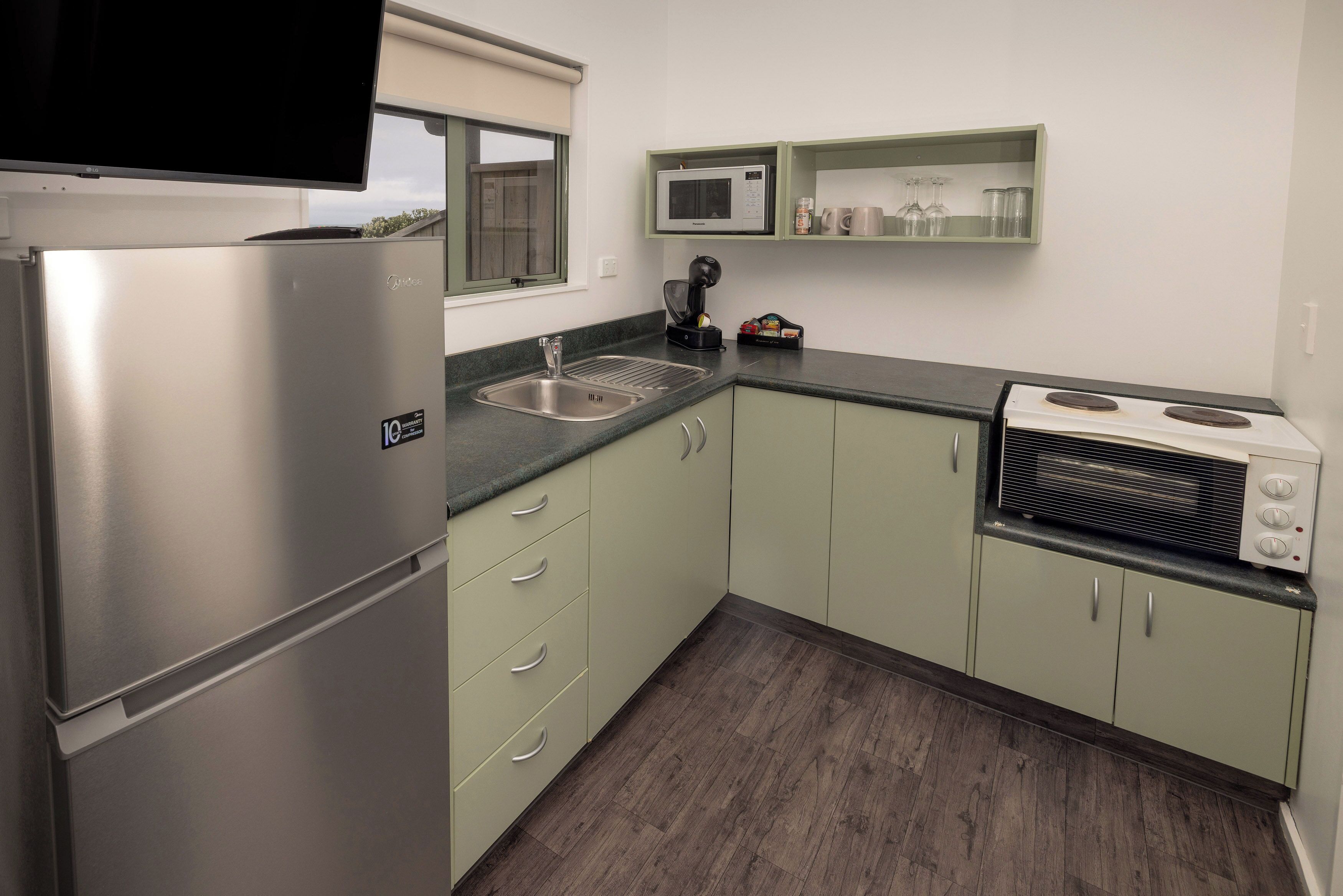 A compact kitchen with a stainless steel refrigerator, a microwave, a stove, and a sink.