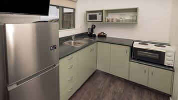 A compact kitchen with a stainless steel refrigerator, a microwave, a stove, and a sink.