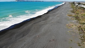 Une plage bordée d’une longue étendue de sable noir, d’une eau turquoise et limpide, et offrant une vue lointaine sur la ville.