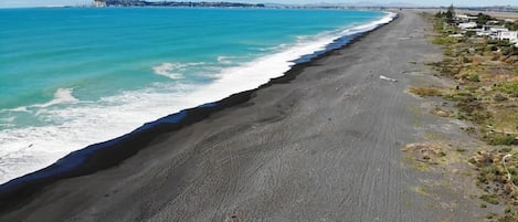 A beach with a long stretch of black sand, clear turquoise water, and a distant cityscape.