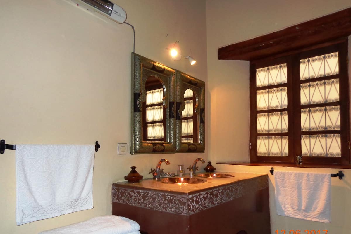 A bathroom with a large mirror, a sink with two faucets, and a window with decorative glass panes.