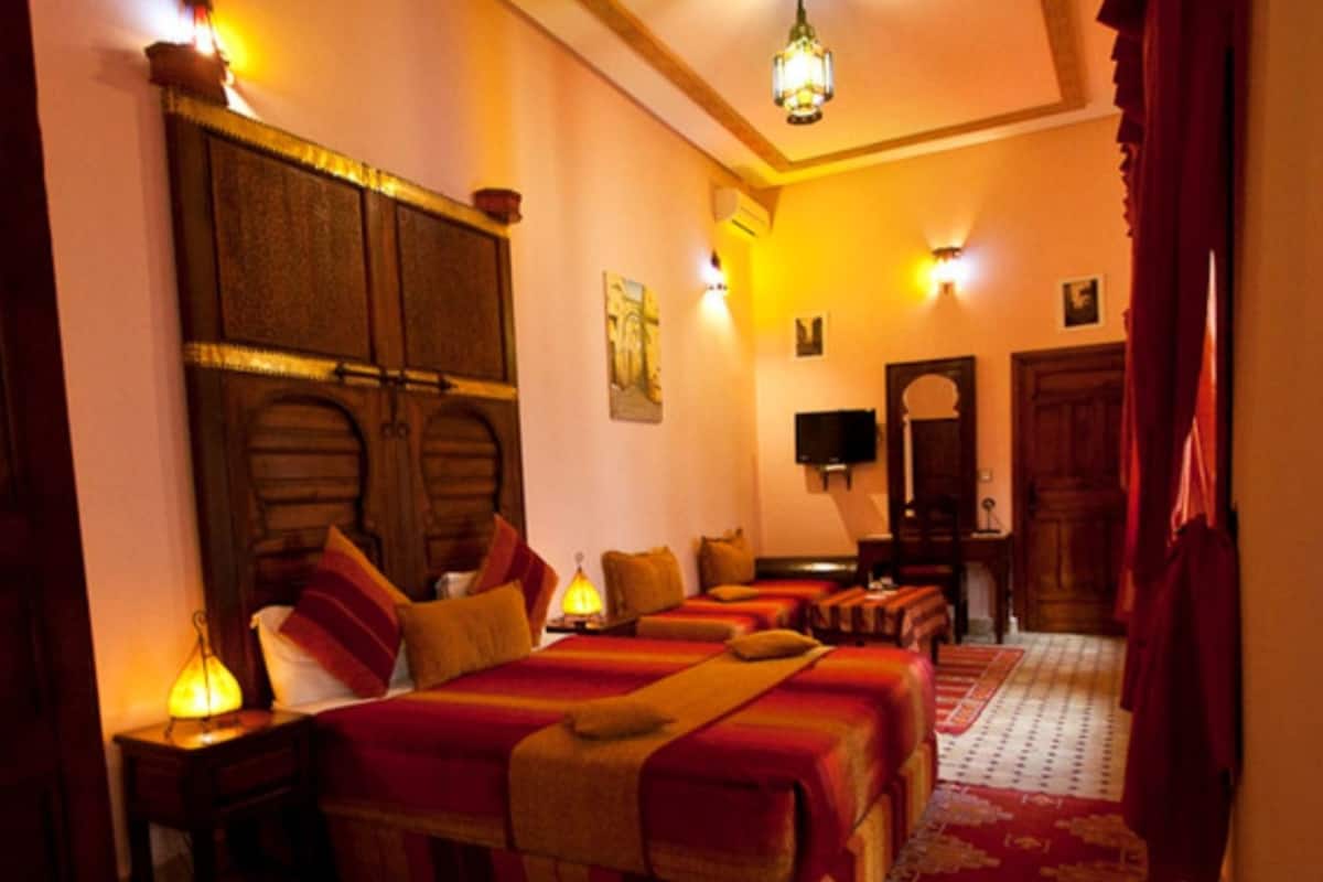 A hotel room with a large bed, two bedside tables, a desk, a chair, a television, and a wardrobe.